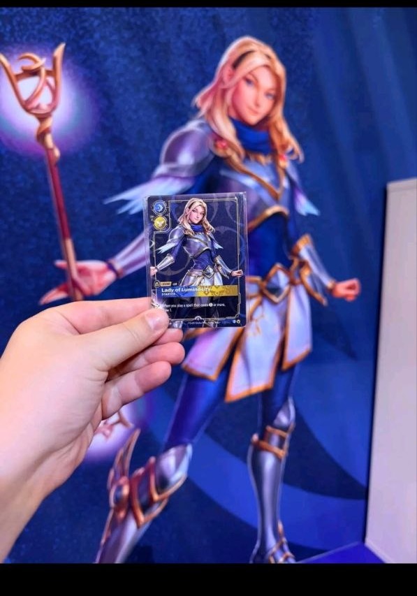 The Lady of Luminosity starter card held in front of the full-figure Lux standee at the Riftbound RQ Utrecht