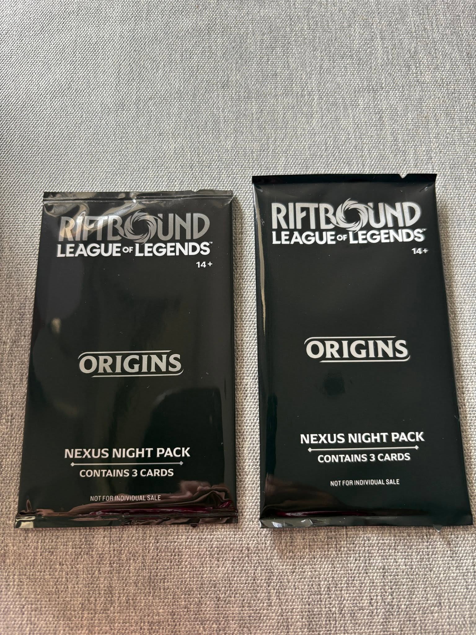 Fronte di due bustine Nexus Night Origins Riftbound: quella di prima edizione a sinistra &egrave; pi&ugrave; corta, la ristampa a destra &egrave; pi&ugrave; lunga