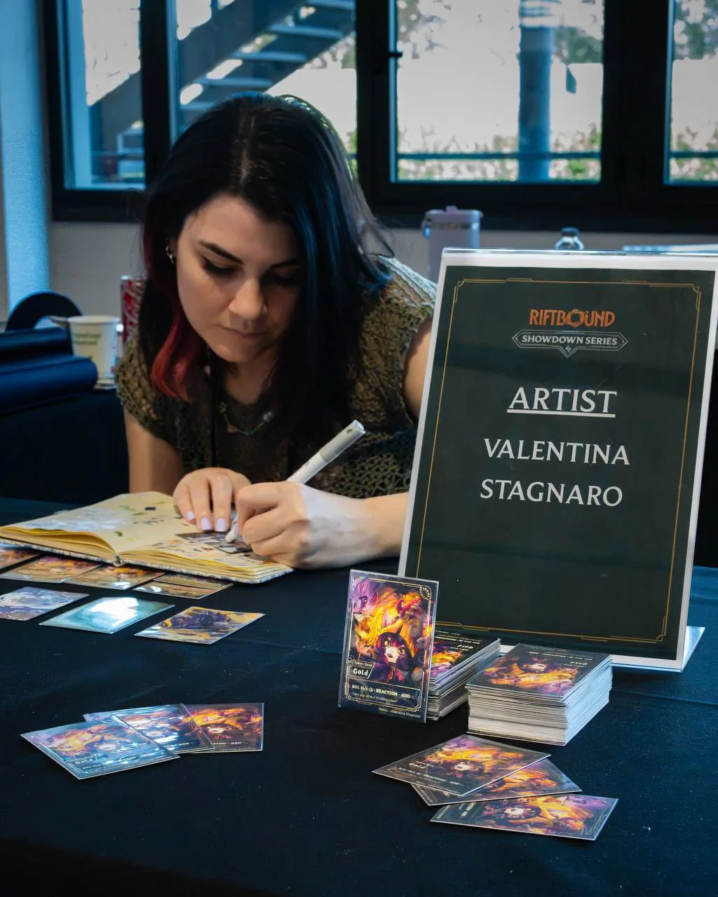 Valentina Stagnaro dipinge una carta al suo tavolo del Riftbound Showdown Series di Lucca, con il cartello «Artist» accanto